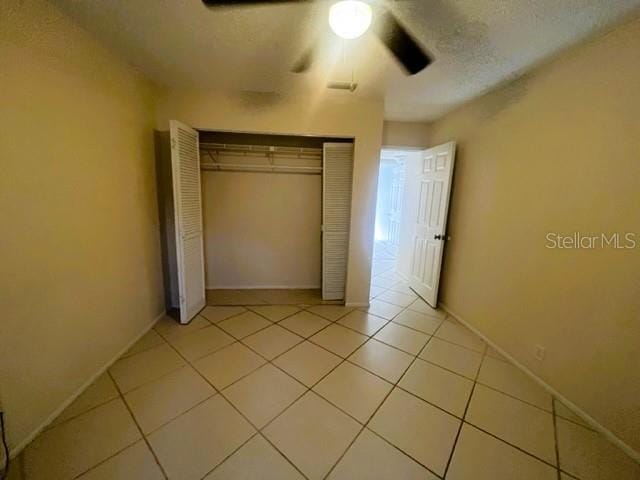 unfurnished bedroom with light tile patterned floors, ceiling fan, and a closet