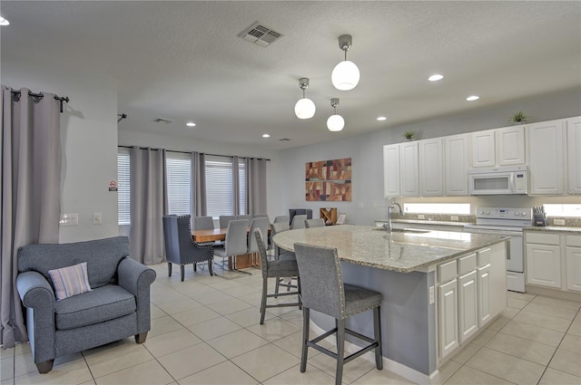 kitchen with sink, white appliances, a kitchen island with sink, white cabinets, and pendant lighting