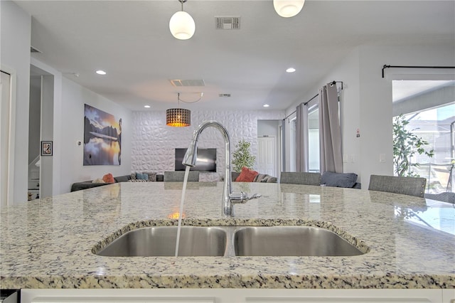 kitchen featuring hanging light fixtures, sink, and light stone counters