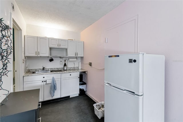 kitchen featuring white refrigerator, white cabinetry, sink, and a textured ceiling