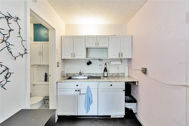 kitchen featuring white cabinetry, light stone countertops, sink, and a textured ceiling