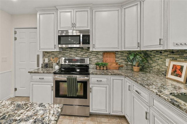 kitchen featuring stainless steel appliances, light stone countertops, white cabinetry, and light tile patterned floors