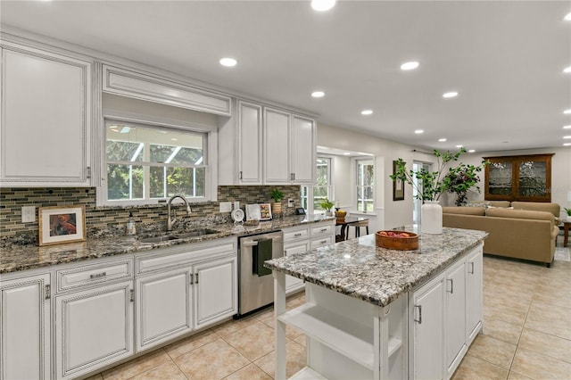 kitchen with stainless steel dishwasher, light stone countertops, white cabinetry, and a kitchen island