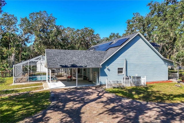 back of house with glass enclosure, a patio area, and a yard