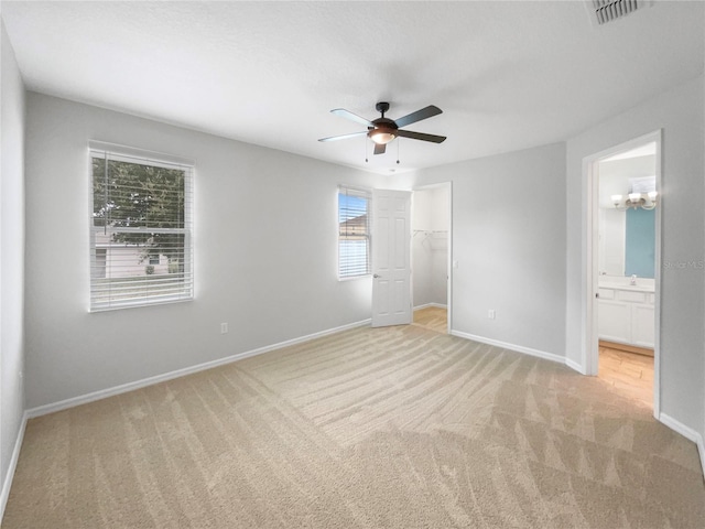 unfurnished bedroom with a closet, a walk in closet, ensuite bath, light colored carpet, and ceiling fan