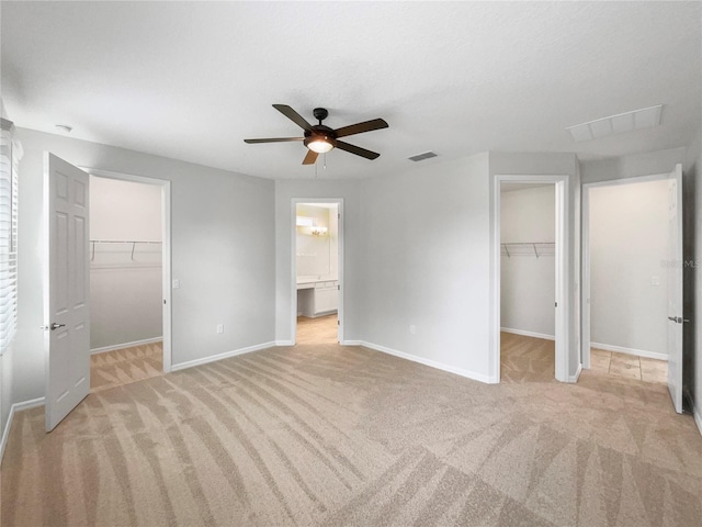 unfurnished bedroom with light carpet, ceiling fan, and a walk in closet