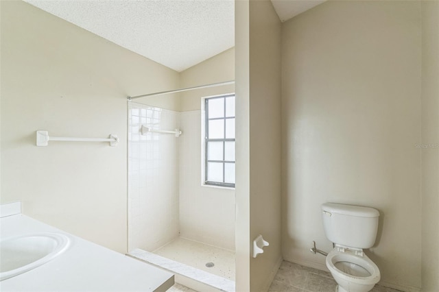 bathroom with a textured ceiling, sink, tiled shower, toilet, and lofted ceiling