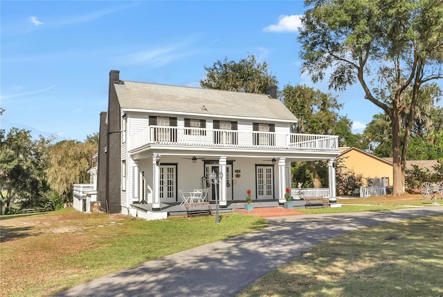 view of front facade with french doors, covered porch, a balcony, a front lawn, and ceiling fan