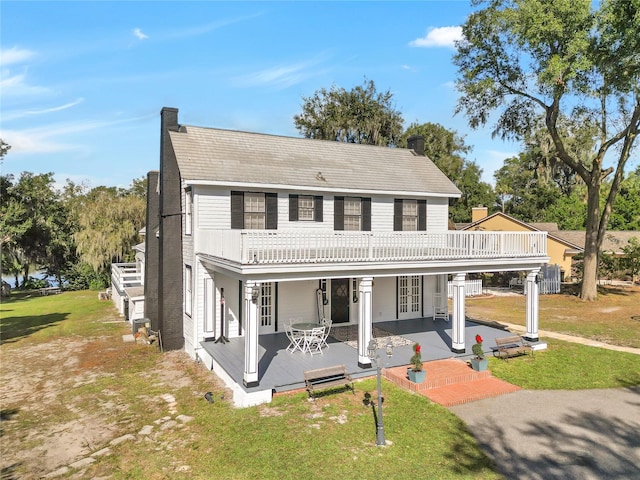 view of front of property featuring a balcony, a front yard, and french doors