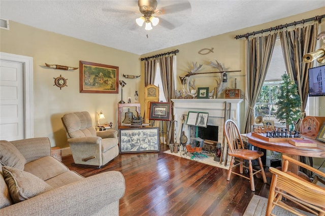 living room with a tiled fireplace, hardwood / wood-style floors, ceiling fan, and a textured ceiling