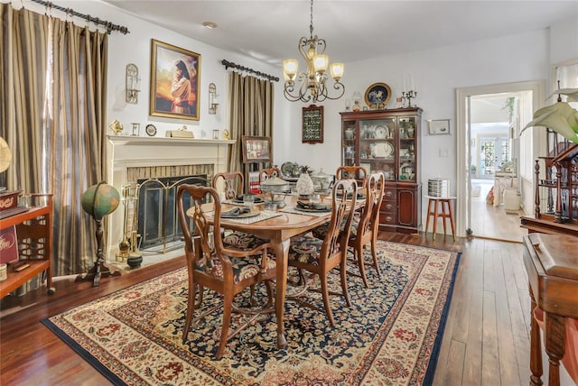 dining area with dark wood-type flooring, a chandelier, and a brick fireplace