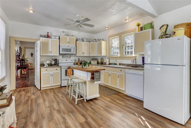 kitchen featuring a center island, a breakfast bar area, butcher block countertops, light hardwood / wood-style flooring, and white appliances