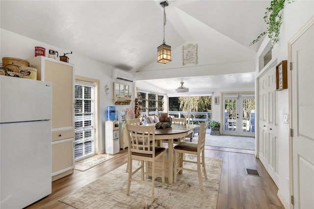 dining area featuring french doors, an AC wall unit, light wood-type flooring, and vaulted ceiling