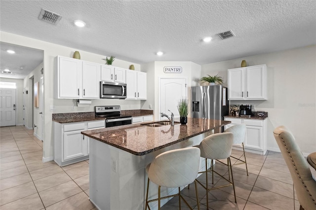 kitchen featuring appliances with stainless steel finishes, white cabinetry, an island with sink, sink, and a kitchen bar