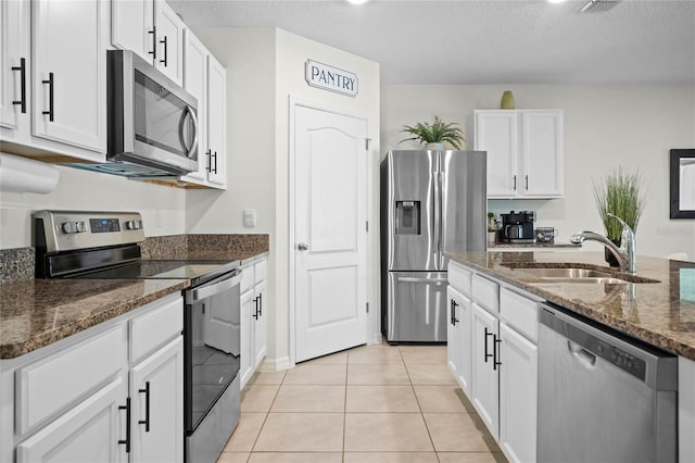 kitchen featuring sink, white cabinetry, light tile patterned floors, dark stone countertops, and stainless steel appliances