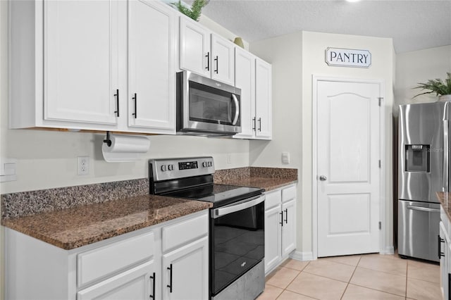 kitchen with light tile patterned flooring, white cabinets, dark stone counters, stainless steel appliances, and a textured ceiling