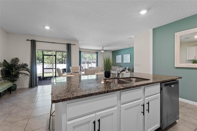 kitchen featuring sink, a center island with sink, dishwasher, dark stone counters, and white cabinets