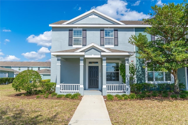 traditional-style home with a porch, a front yard, and stucco siding