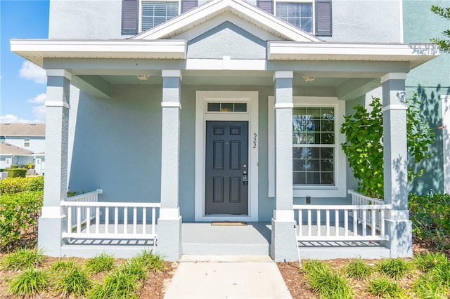 doorway to property with covered porch and stucco siding