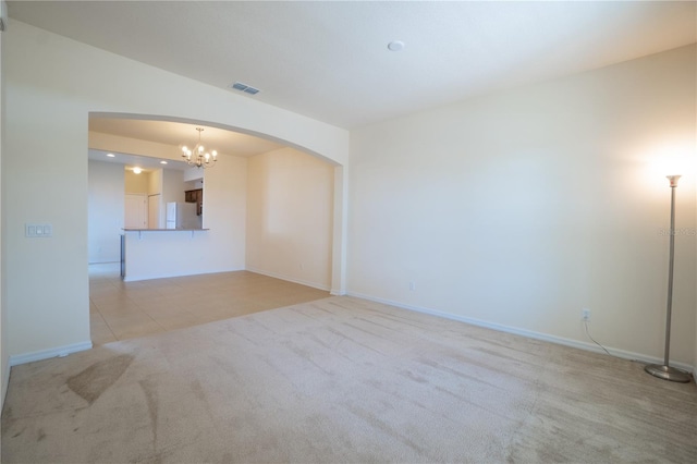 spare room featuring arched walkways, a notable chandelier, visible vents, light carpet, and baseboards