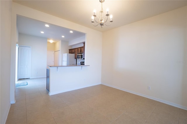 kitchen with a notable chandelier, stainless steel microwave, freestanding refrigerator, a peninsula, and baseboards