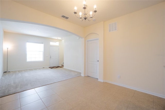 spare room with visible vents, arched walkways, light colored carpet, stairway, and a chandelier