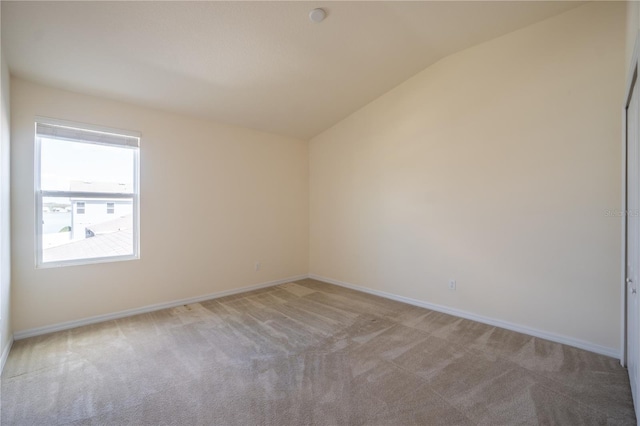 carpeted spare room featuring baseboards and vaulted ceiling