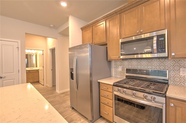 kitchen featuring light wood-type flooring, light stone countertops, decorative backsplash, and appliances with stainless steel finishes