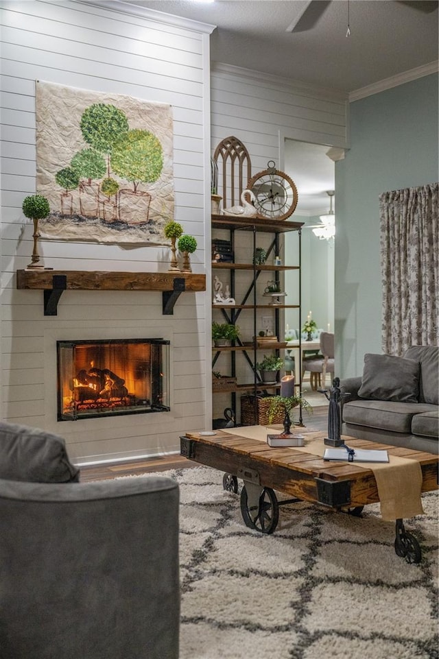 living room with a large fireplace, ceiling fan, crown molding, and wood walls