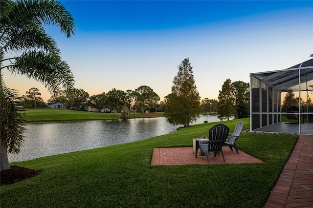 yard at dusk featuring a lanai, a patio area, and a water view