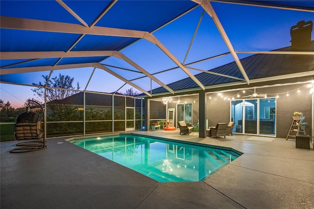 pool at dusk featuring a patio, glass enclosure, and ceiling fan