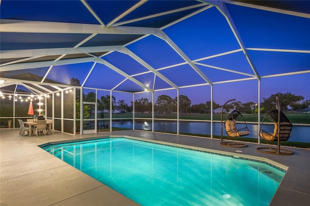 pool at dusk with a lanai, a patio area, and a water view