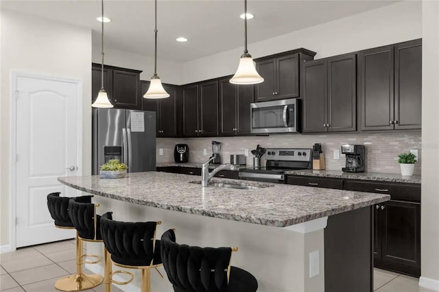 kitchen featuring a center island with sink, a kitchen breakfast bar, backsplash, pendant lighting, and appliances with stainless steel finishes