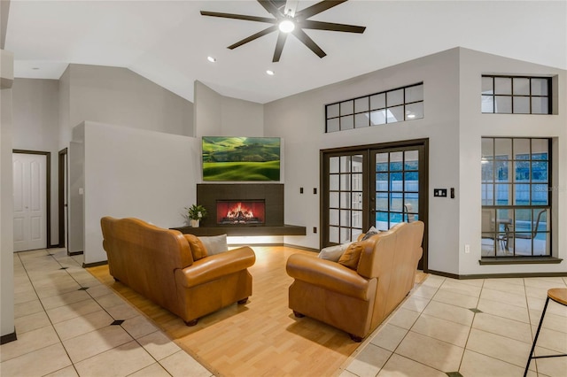 living room with french doors, light tile patterned floors, high vaulted ceiling, a tiled fireplace, and ceiling fan