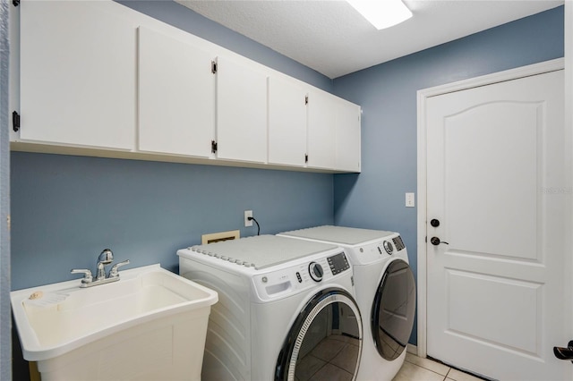 clothes washing area featuring cabinets, sink, a textured ceiling, light tile patterned floors, and washing machine and clothes dryer