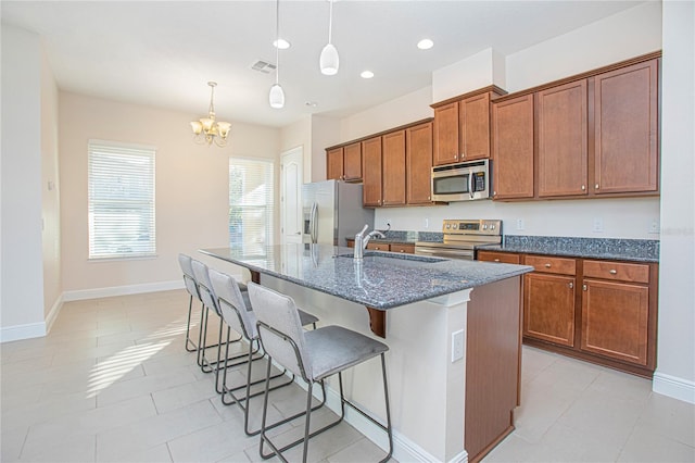 kitchen with a kitchen bar, appliances with stainless steel finishes, sink, a center island with sink, and hanging light fixtures