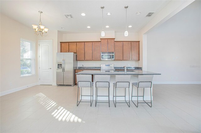 kitchen featuring appliances with stainless steel finishes, a breakfast bar, a kitchen island with sink, sink, and decorative light fixtures