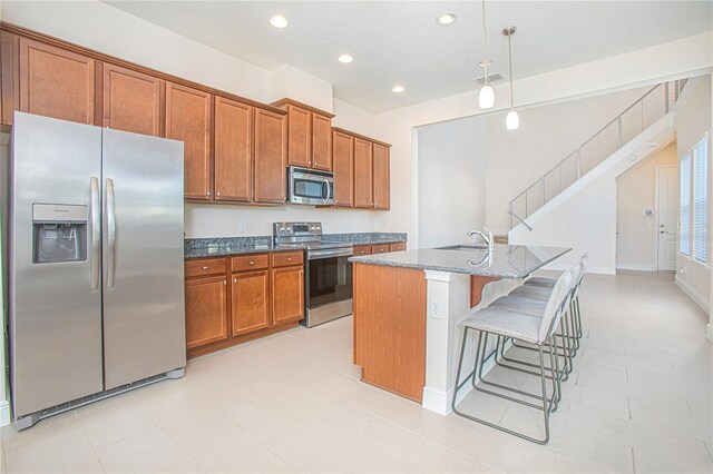 kitchen featuring a kitchen breakfast bar, dark stone counters, stainless steel appliances, a kitchen island with sink, and hanging light fixtures