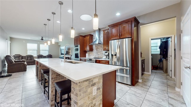 kitchen featuring stainless steel appliances, hanging light fixtures, a breakfast bar, wall chimney exhaust hood, and ceiling fan