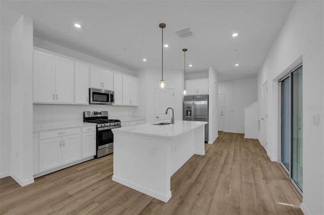 kitchen featuring sink, white cabinetry, stainless steel appliances, a center island with sink, and decorative light fixtures