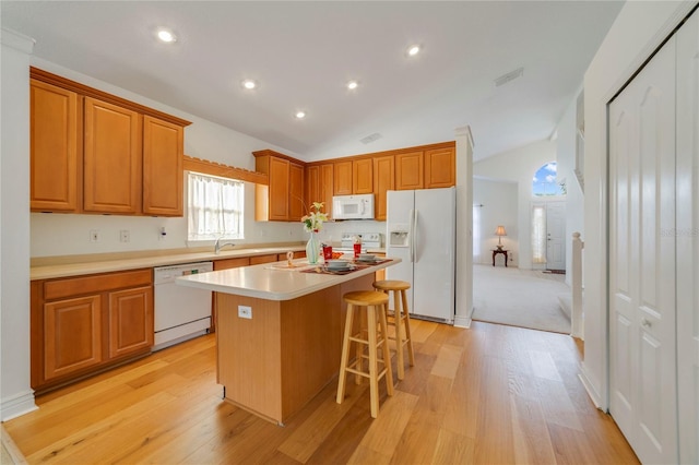 kitchen featuring a center island, vaulted ceiling, a breakfast bar area, light hardwood / wood-style flooring, and white appliances