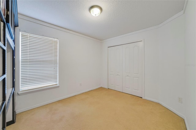 unfurnished bedroom with light carpet, a closet, a textured ceiling, and ornamental molding