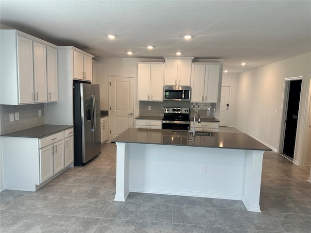 kitchen with tasteful backsplash, white cabinetry, appliances with stainless steel finishes, and a center island with sink