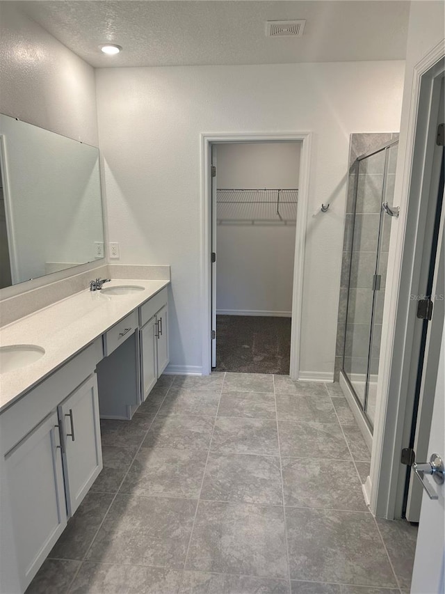 bathroom featuring vanity, tile patterned flooring, a shower with door, and a textured ceiling