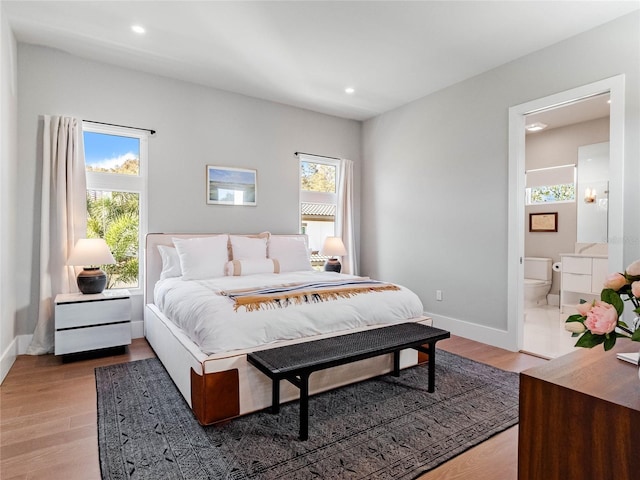 bedroom with light wood-type flooring, ensuite bathroom, and multiple windows