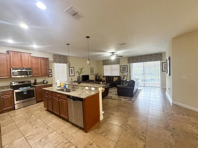 kitchen featuring ceiling fan, sink, stainless steel appliances, an island with sink, and decorative light fixtures