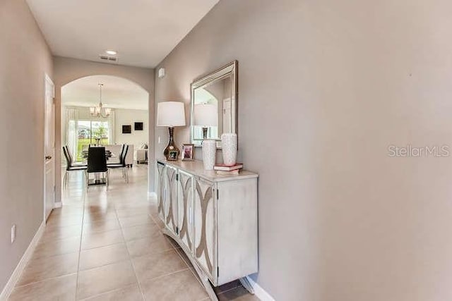 hall featuring arched walkways, light tile patterned flooring, visible vents, and baseboards