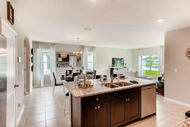 kitchen with light tile patterned flooring, a kitchen island with sink, a sink, open floor plan, and stainless steel dishwasher