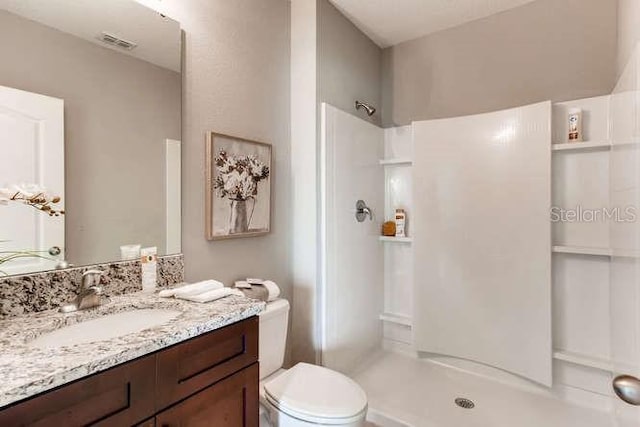 bathroom with visible vents, vanity, toilet, and a walk in shower