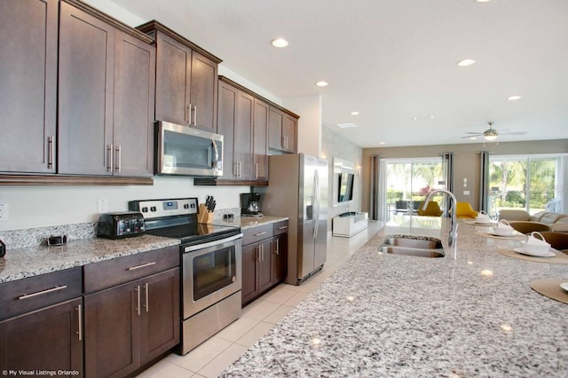 kitchen featuring dark brown cabinetry, sink, appliances with stainless steel finishes, light stone countertops, and light tile patterned floors